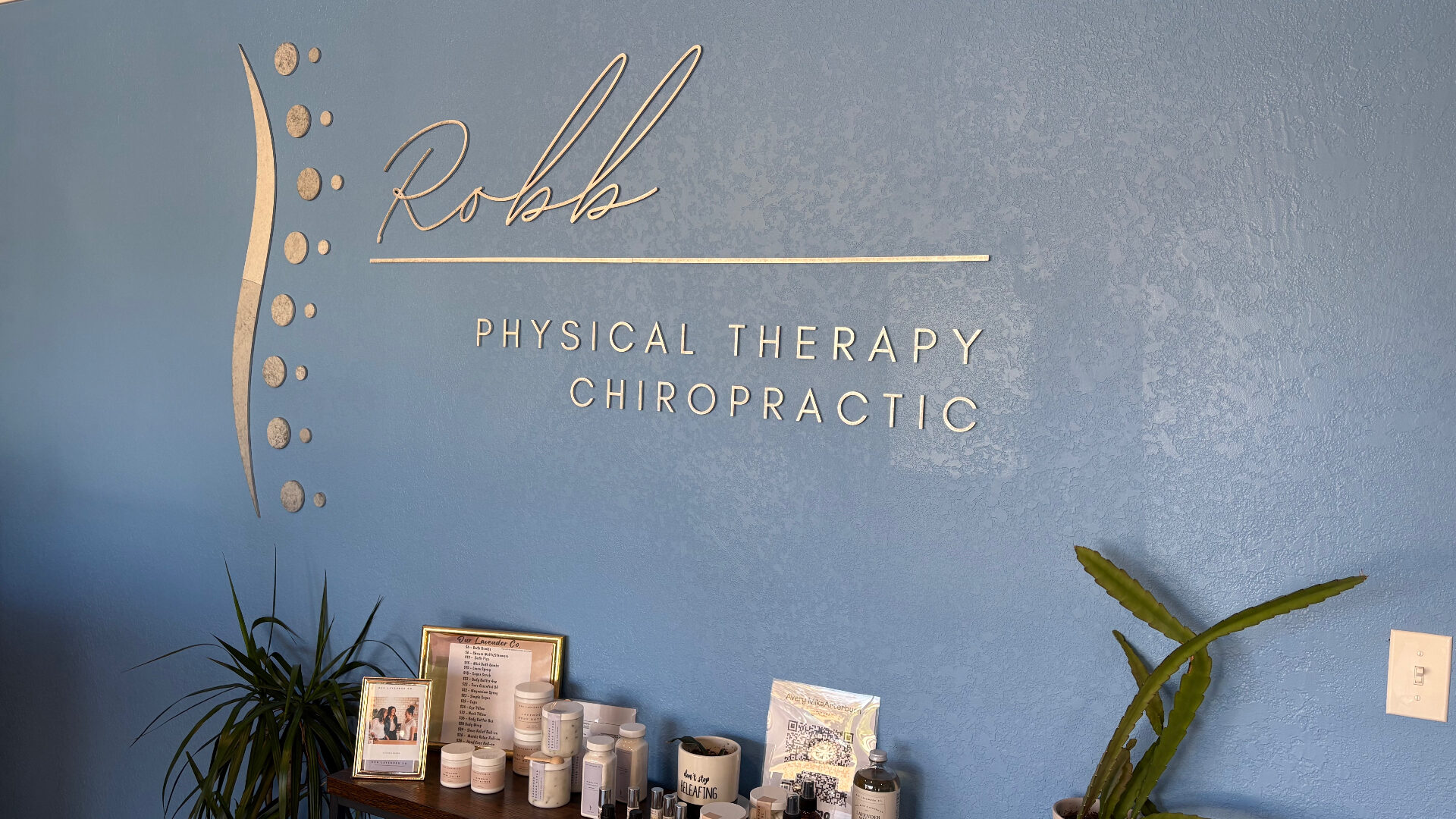 Robb Physical Therapy & Chiropractic gold signage on a blue clinic wall above a wellness product display in Sidney, Nebraska